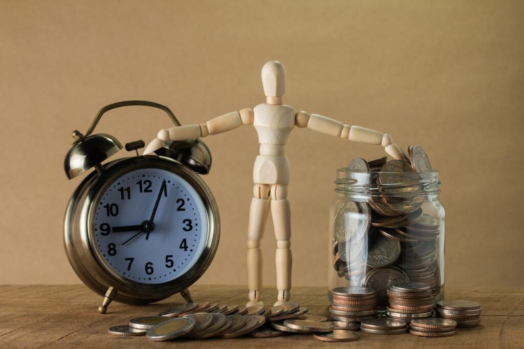 A wooden doll toy standing between an alarm clock and a jar full of change to illustrate free-to-play games relationship with time and money